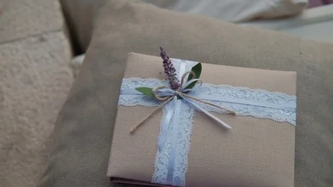 Gift in tissue package with delicate ribbon and flower lies on pillow in room. Stock Footage 82240798