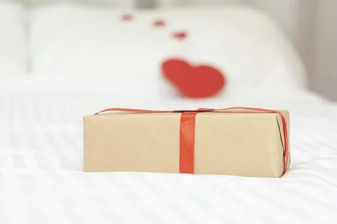 A gift on a white background. A gift on the bed. Hearts in the background. Stock Photos