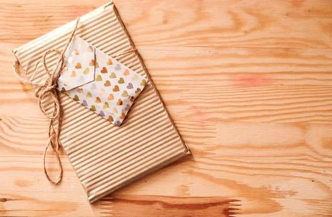 Gift-wrapped package with decorative envelope on a rustic wooden background Stock Photos