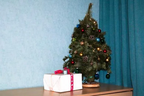 A gift wrapped in silver paper under decorated Christmas tree at home. New Year. Stock Photos