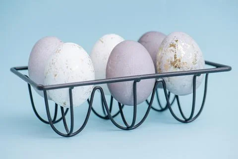 Gilded easter eggs and regular ones on a metal egg holder over blue background. Stock Photos