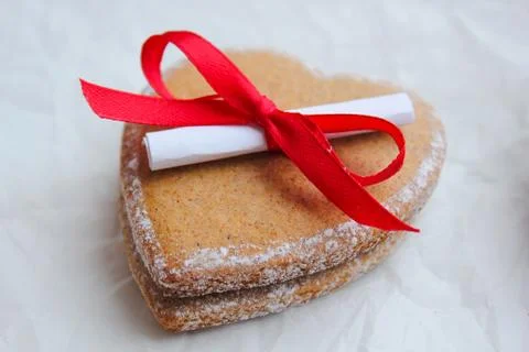 Ginger biscuits in the shape of a heart with a note and a red bow Stock Photos