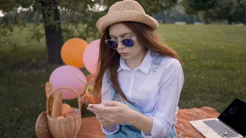 Ginger college student in straw hat and sunglasses texts and smiling in park 스톡 동영상 95247222
