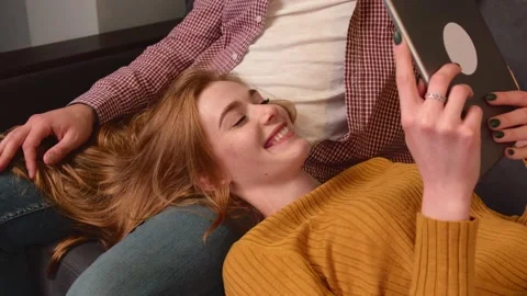 Ginger lady with freckles is smiling while lying on her lovers knees and using a Stock Footage 146582615