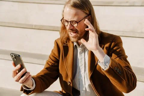 Ginger man gesturing and using mobile phone while sitting on stairs Stock Photos