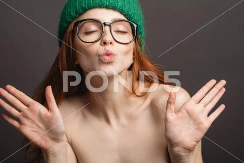 Ginger woman wearing glasses and green hat pouting her lips ready for kiss Stock Photos