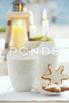 Gingerbread Stars With White Icing And White Cups In Front Of Candles