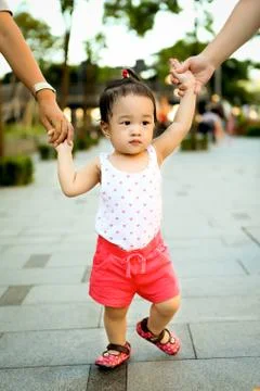 Girl (2-3) walking while adults hold her hands Stock Photos