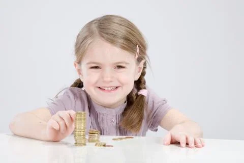 Girl (4-5) counting stack of coins, smiling, portrait 스톡 사진