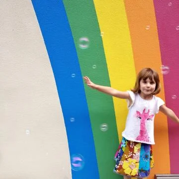 Girl (4-5) dancing with bubble in front of painted rainbow Stock Photos