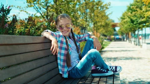 Girl 7-8 years sitting on the bench and smiling at camera Stock Footage