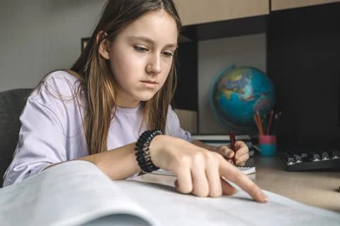 The girl is actively taking notes in notebook for homework, sitting in her ro Stock Photos