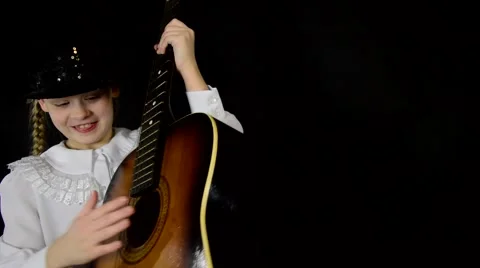 Girl actress is trying to play the guitar in a white dress on a black Stock Footage 59450079