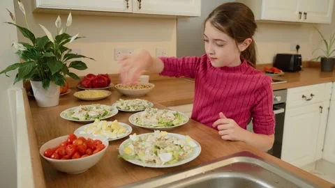 Girl adding eggs to salad plates. Kid placing boiled egg pieces on salad Stock Footage 312042255