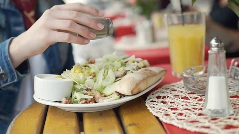 Girl adding pepper to her salad and eating it in the outdoor cafe, steadycam sho Stock Footage