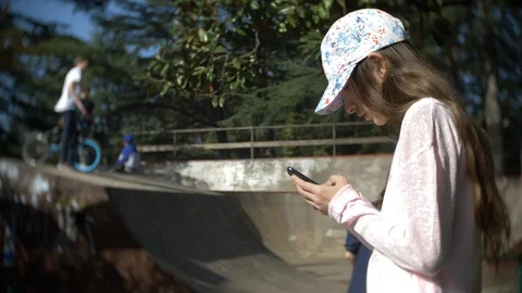 A girl alone using a mobile phone outdoors. while other children have active Stock Footage 88337537