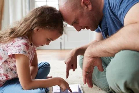 Girl and dad sit on the floor playing with tablet, close up Stock Photos