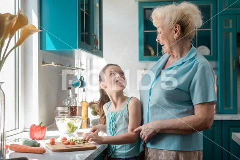 Girl and granny having fun in the kitchen, cooking a meal with homegrown veggies Stock Photos