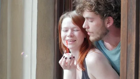 Girl and guy blowing bubbles out the window Видео 73533984
