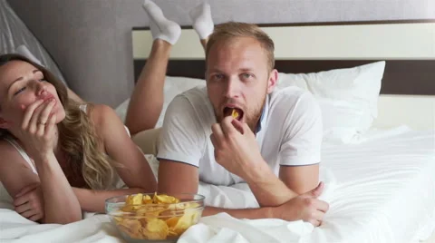 The girl and the guy eating chips lying on the bed Stock Footage 65204875