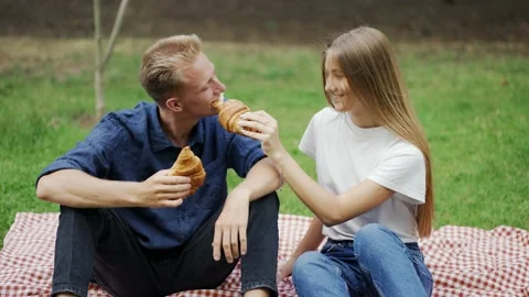 A girl and a guy feed each other a croissant at a picnic as a couple. romantic Vídeo Stock 213174103