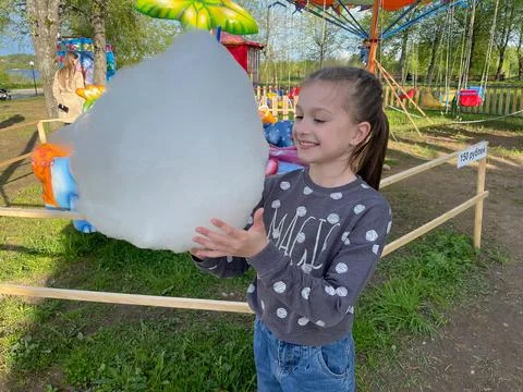 The girl appetizingly eats cotton candy against the background of attractions Stock Photos