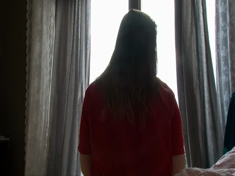 Girl applying makeup on in front of large window with curtains, back view 스톡 동영상 72853225