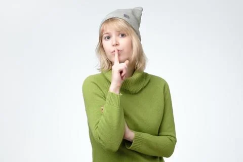 Girl asks to keep secret information confidential, dressed in green sweater and Stock Photos