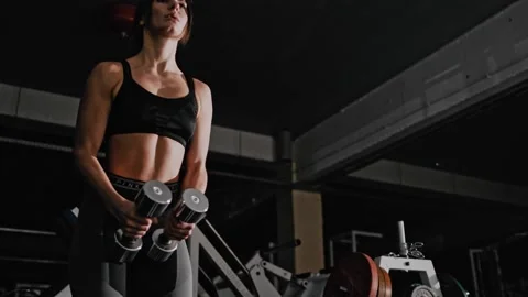 A girl of athletic physique trains in the hall. Standing breeding dumbbells Stock Footage