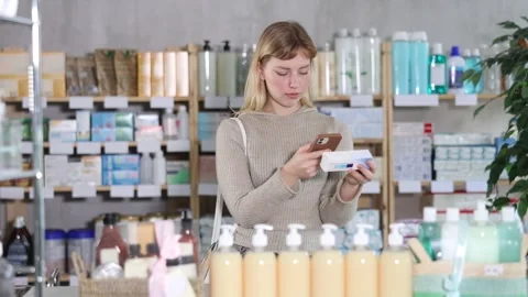 Girl in autumn clothes scans code on package of ointment to check the expiration Stock Footage 312630726