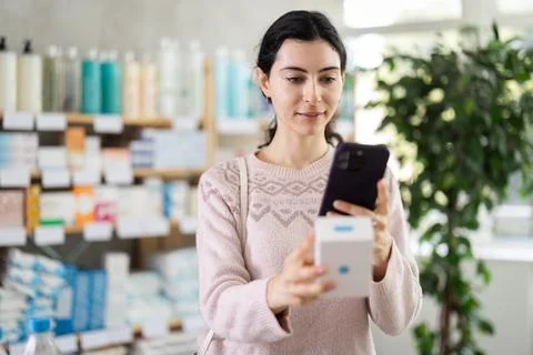 Girl in autumn clothes scans code on package of pills to check expiration date Foto stock