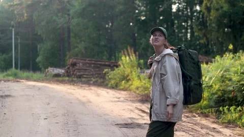A girl with a backpack came out of the forest onto a country road Stock Footage 201603502