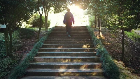 Girl with backpack climbs up stone steps of old staircase in green park or Video stock 222016143