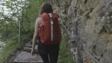 Girl with the backpack is going up through the  thin path next to the rock Stock Footage 83525033