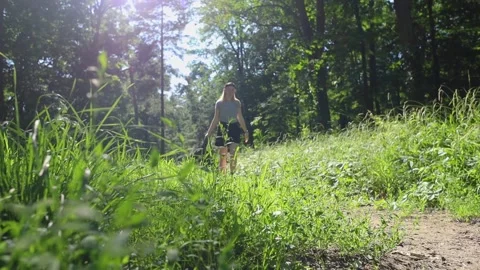 Girl with backpack on her back walks along path in forest. Short shorts, white T Stock Footage 247360332