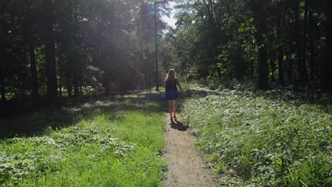 Girl with backpack on her back walks along path in forest. Short shorts, white T Video stock 247360344