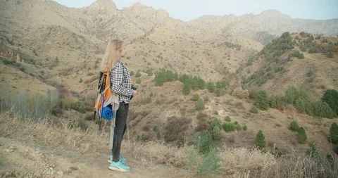 Girl with a backpack, looking through binoculars in the mountains in the fall. 4 Stock Footage 98776783