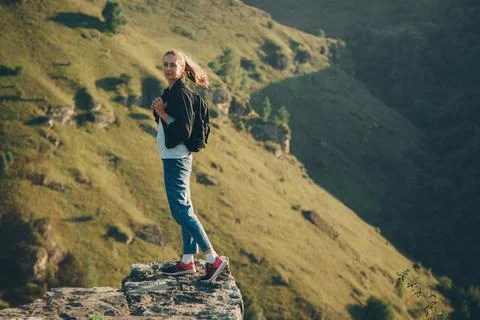 A girl with a backpack stands on the edge of a cliff. Journey through the mou 스톡 사진