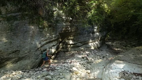 Girl with a backpack walking alone through a beautiful mountain river canyon Stock Footage 253889570