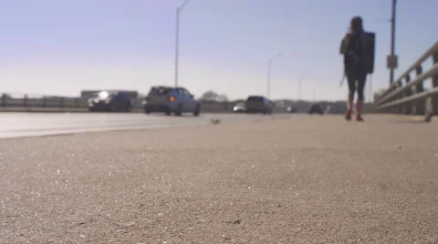 Girl with a backpack walking away down a sidewalk, cars driving by Stock Footage