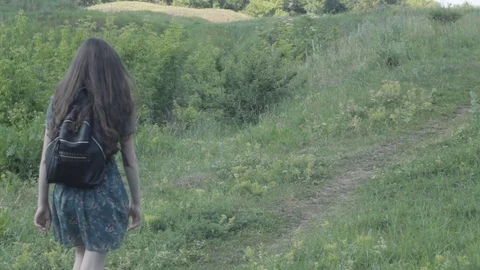A girl with a backpack walks through the meadows Stock Footage