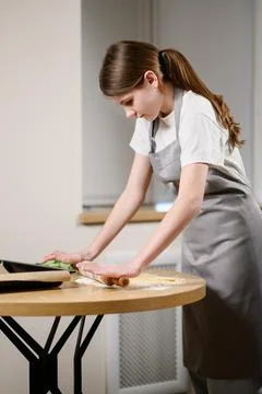 Girl bakes bread on rustic table, rolling out dough on countertop. Teenager Stock Photos