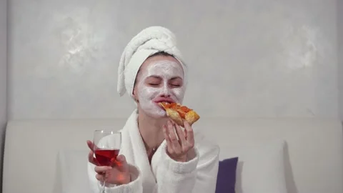 Girl in a bathrobe, with a mask for the face eats pizza and drinks wine Stock Footage 153420158