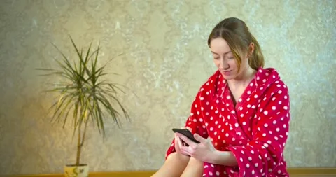 Girl in a bathrobe, using a smartphone for work at home and reading news and Stock Footage 130282812
