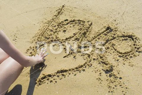 Girl at the beach drawing hearts on a sand Stock Photos