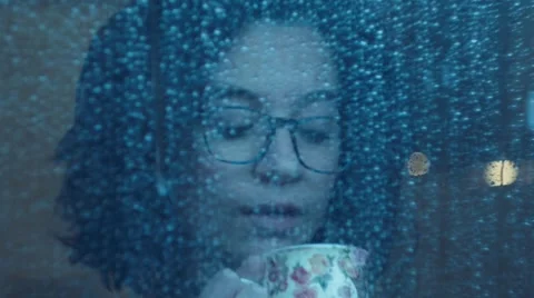 Girl behind window drinking an hot drink cup  in a rainy day. Shot in slowmotion 動画素材 47874523