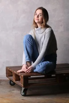 Girl with bended knee sitting on a deck. Gray background Stock Photos