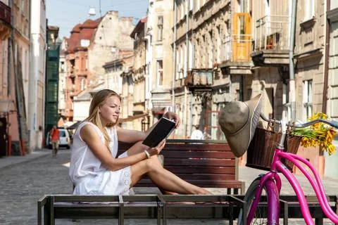 Girl with bicycle sitting on bench and reading book Stock Photos