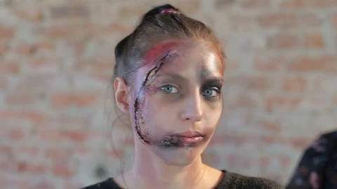Girl with big eyes whose face has wax plastic makeup in form of bloody wound Video stock 105600007