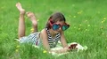 Girl in big sunglasses in the shape of hearts with red smartphone lies on grass HD Footage